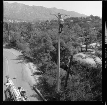 Linemen clearing tree growth around distribution lines and poles with chain saw from bucket truck