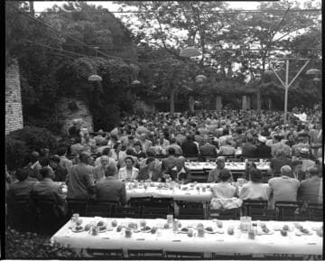 Hundreds of people seated at tables at picnic eating
