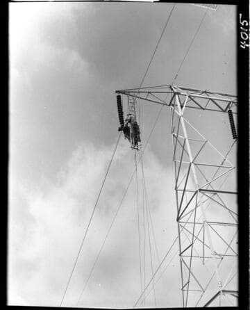 Men hanging from tower crossarm stringing conductor