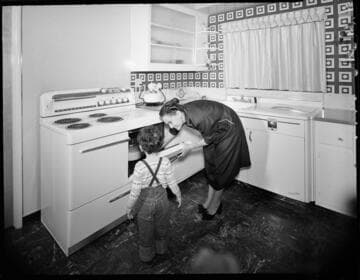 Residential kitchen with woman checking roast in electric oven