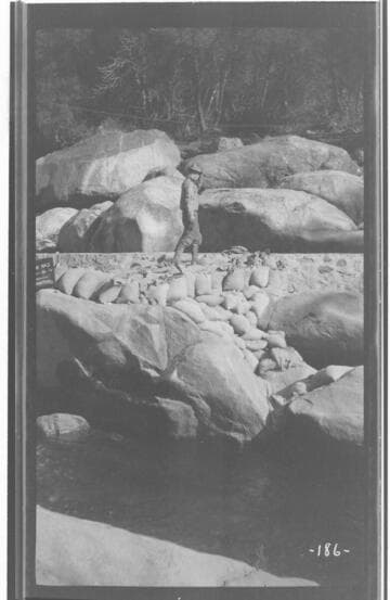 A man is walking along the rocks at the construction site of the Marble Fork dam at Kaweah #3 Hydro Plant