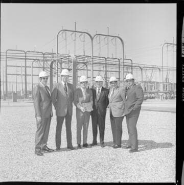 Men in suits (with and without hardhats) receiving a plaque or award at a transmission substation