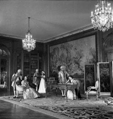 Six people in period costume in the west end of the library of the Huntington residence